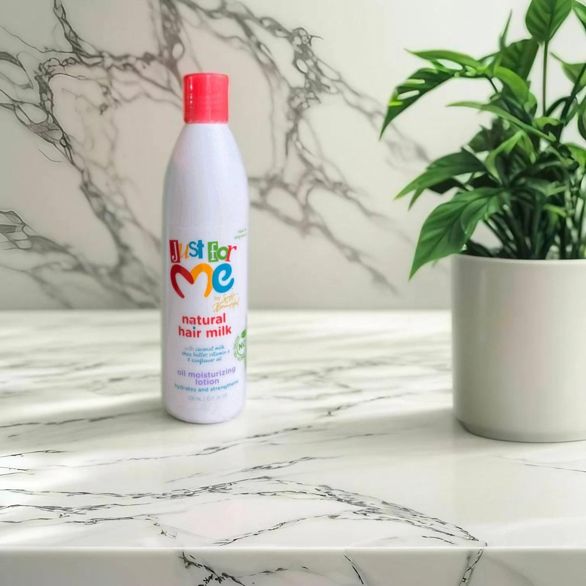 Just for Me Natural Hair Milk moisturizing lotion bottle placed on a marble countertop, next to a potted plant, showcasing its vibrant packaging.